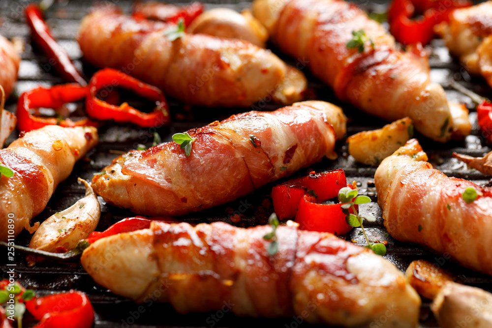 Spicy chicken meat, Grilled chicken tenderloin wrapped with bacon with addition chili peppers, garlic and herbs on grill plate, close-up