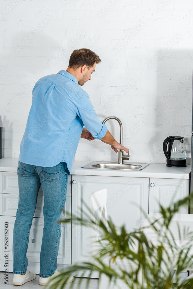 back view of man in casual clothes washing hands in kitchen back view of man in casual clothes washing hands in kitchen