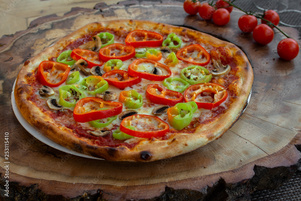 Pizza with tomato sauce, ham, egg, fresh green and red peppers, yellow cheese, olive oil and basil. On a wooden board against the background of cherry tomatoes.
