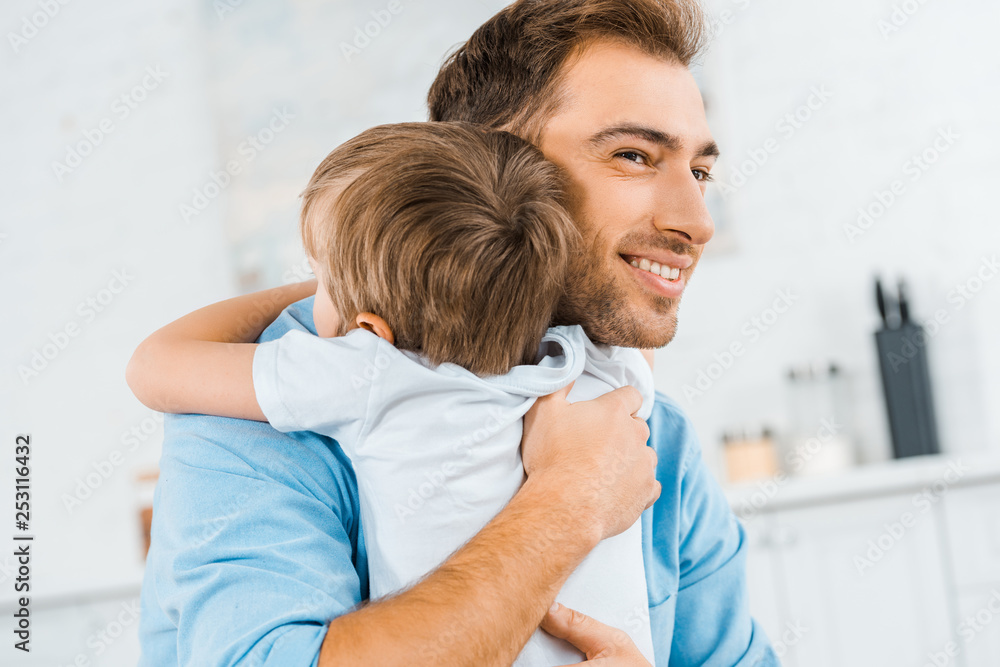 Fototapeta premium smiling handsome father hugging preschooler son at home
