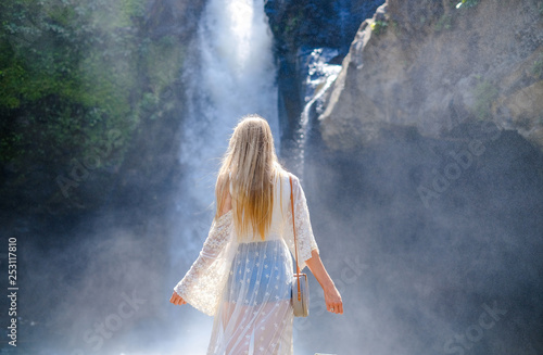 The blonde girl stands with her hands spread against the background of a violent waterfall
