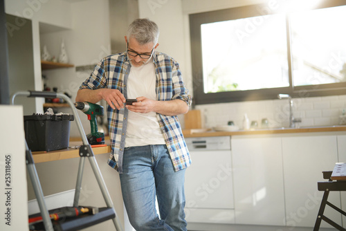 Handyman checking cellphone leaning on ladder in modern kitchen