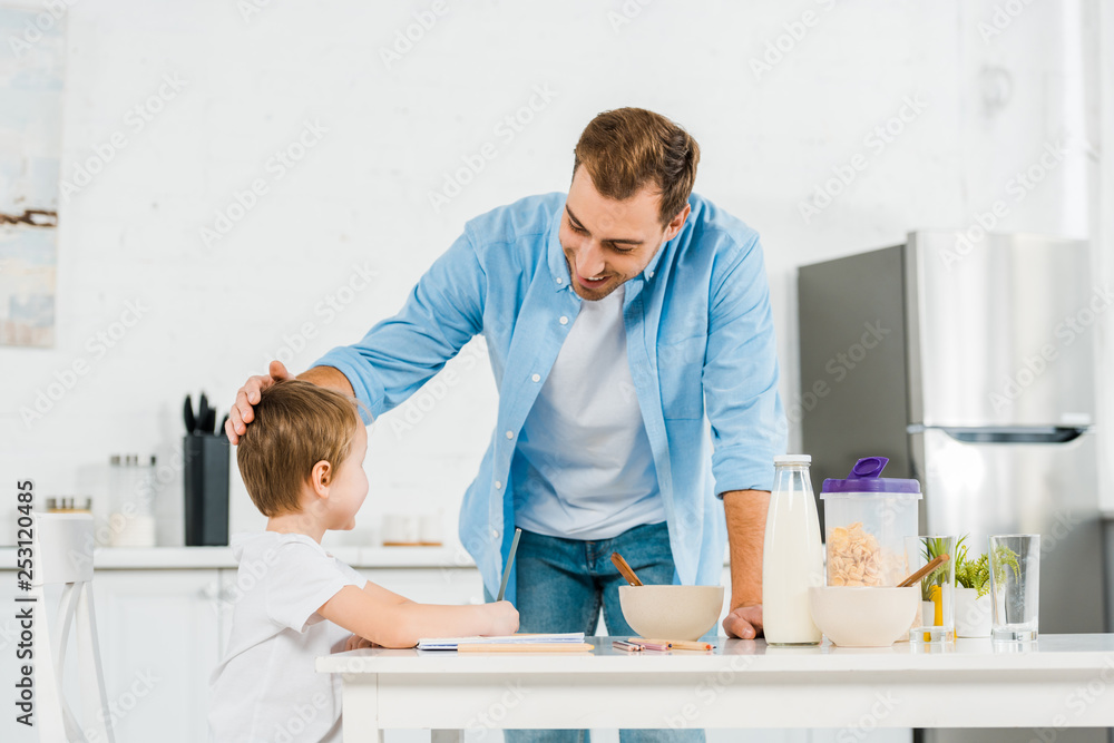 Fototapeta premium smiling father stroking preschooler son during breakfast in kitchen