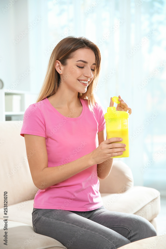 Young woman with bottle of protein shake sitting on sofa at home Young woman with bottle of protein shake sitting on sofa at home