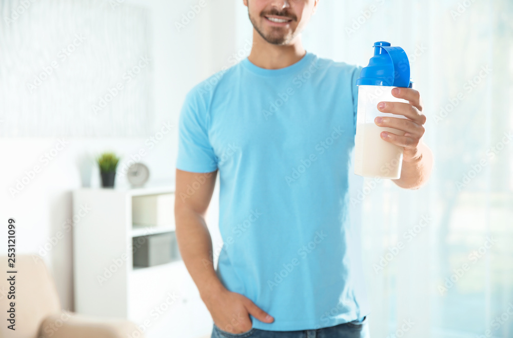 Young man with bottle of protein shake at home, closeup Young man with bottle of protein shake at home, closeup