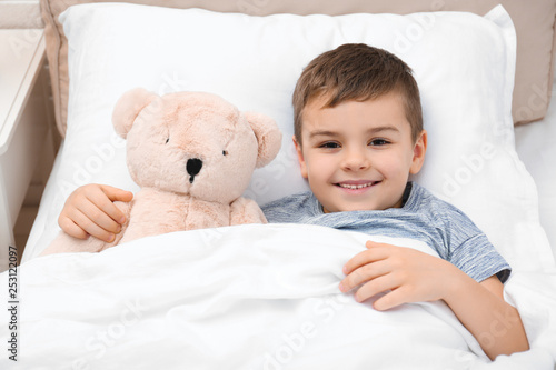 Cute child with teddy bear resting in bed at hospital