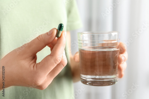 Woman holding spirulina pill and glass of water, closeup