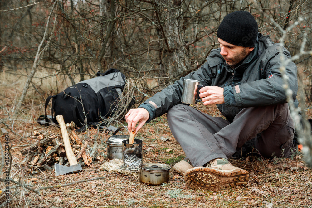 man relaxing in the forest camping, near the wood stove, utensils and axe with firewoods
