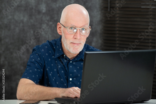 senior man with beard and blue shirt in the office using laptop