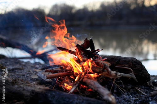 Flame red bonfire and smoke by the river in the evening forest in spring