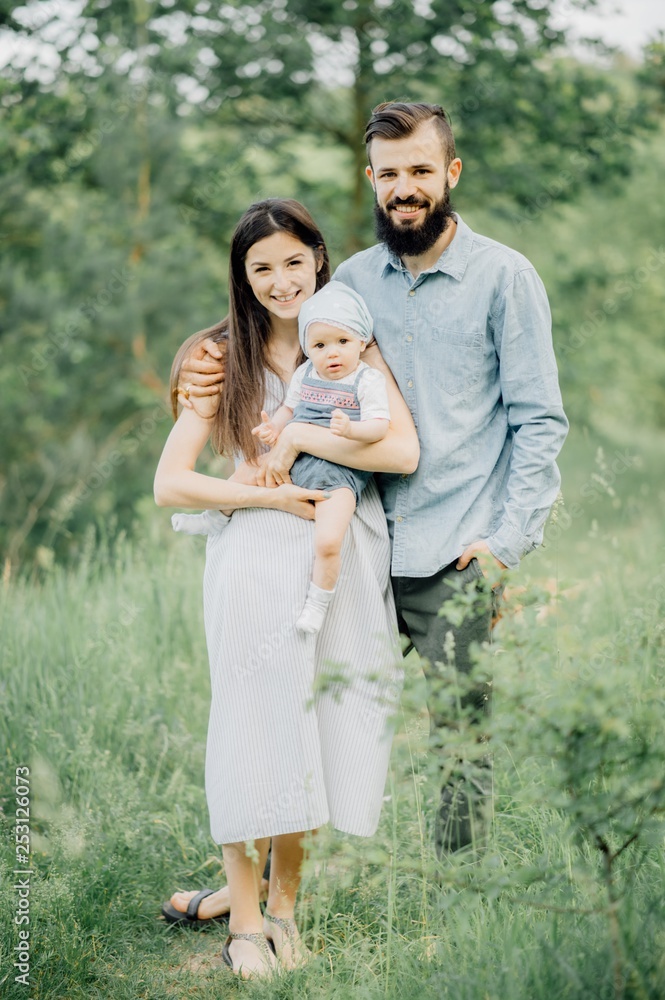 Happy family outdoor in spring. A stylish father with a beard keeps a daughter in his arms with his wife Happy family outdoor in spring. A stylish father with a beard keeps a daughter in his arms with his wife