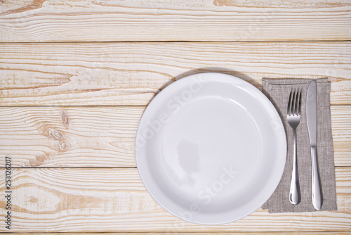 Empty white plate and cutlery on a wooden background, top view.