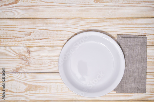 Empty white plate and gray napkin on a wooden background, top view.