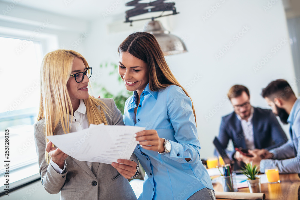 Portrait of two young businesswoman while colleague in background Portrait of two young businesswoman while colleague in background