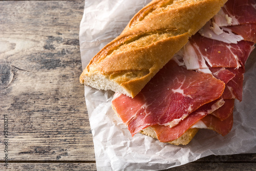 Spanish serrano ham sandwich on wooden table. Copyspace