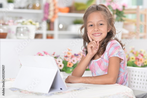 Portrait of little girl sitting at table and using modern tablet