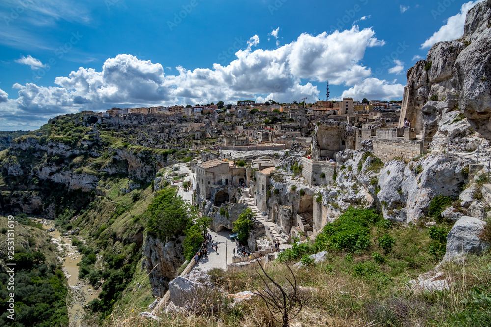 MATERA, ITALY - AUGUST 27, 2018: Warm scenery summer day view of the amazing ancient town of the famous Sassi with white puffy clouds moving on the Italian blue sky over the wonderful buildings