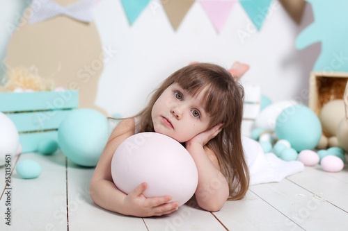 Easter 2019 Close-up portrait of a beautiful little girl's face. Many different colorful Easter eggs, colorful Easter interior. Easter bunny and carrot. The girl is lying with a large ostrich egg 
