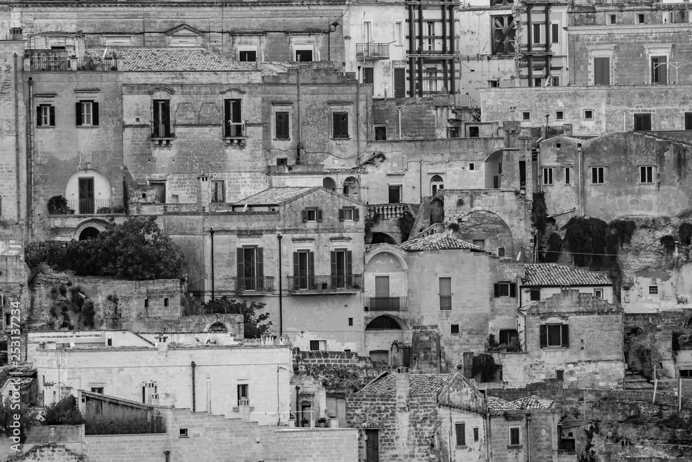 MATERA, ITALY - AUGUST 26, 2018: Tourists and local people look very small walking the narrow city streets of the ancient establishment as seen from far away the hills across in the summer afternoon
