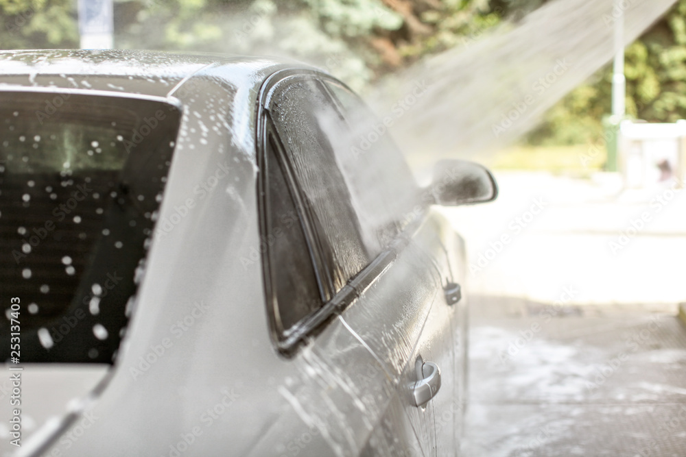 Water spraying from high pressure hose to side window of car washed in self serve carwash.