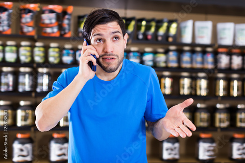 Glad man talking by phone near shelves in shop