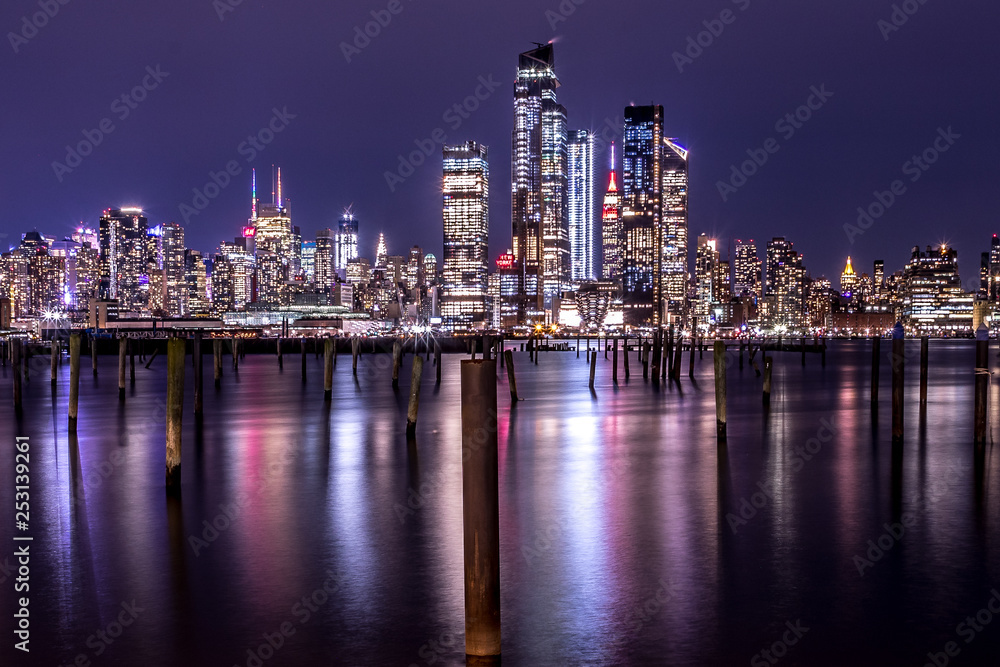 New York City Manhattan Midtown Panorama at Night with Skyscrapers illuminated over Hudson River.