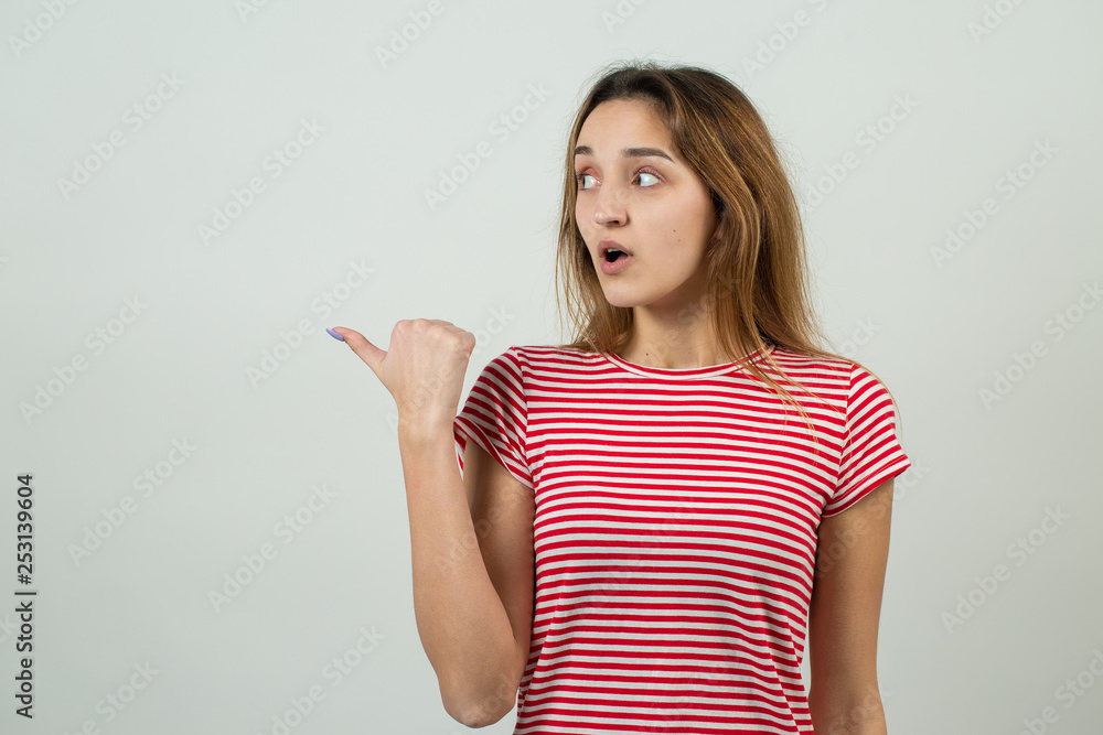 Happy young caucasian female in a striped red T-shirt pointing fingers away, showing copy space for your text. Happy young caucasian female in a striped red T-shirt pointing fingers away, showing copy space for your text.