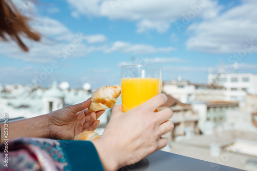 Beautiful young woman standing on balcony , drinking juice and eating croissant. Close up