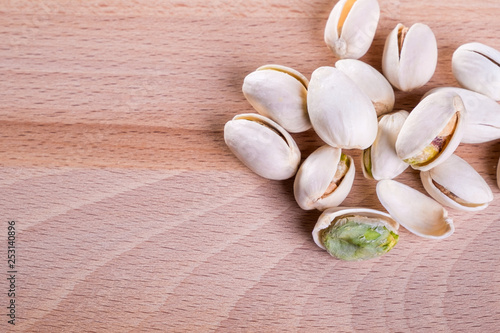 Close up Pistachio nuts with shell on wooden floor background. © Sitthikorn