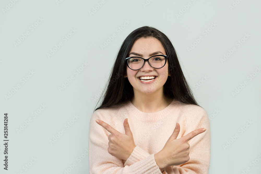 Happy young caucasian female in glasses in a pink jumper pointing fingers away, showing copy space for your text. Happy young caucasian female in glasses in a pink jumper pointing fingers away, showing copy space for your text.