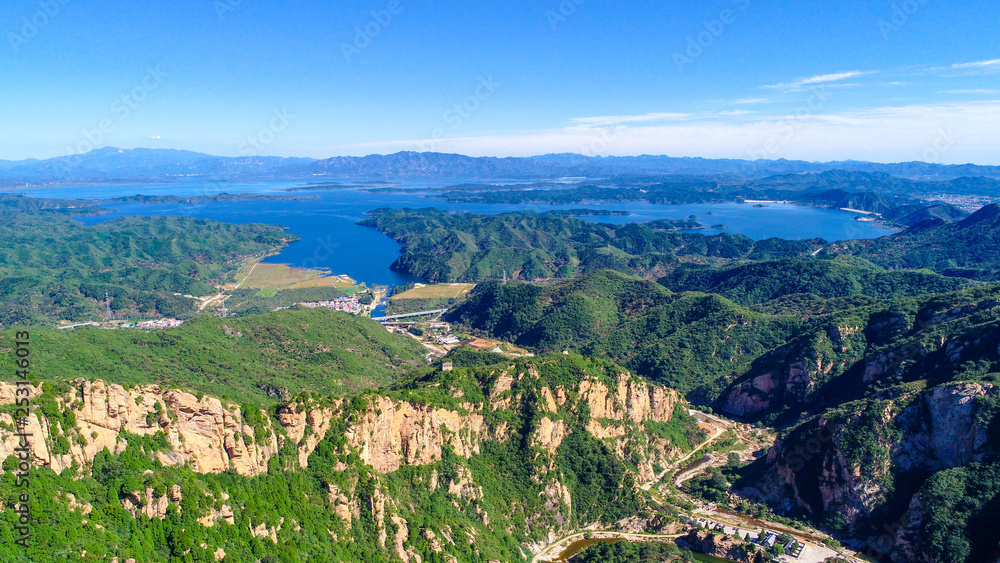 Obraz premium Aerial view of mountain with water reservoir on the background. Mountain peak with beautiful blue sky and green forest. Landscape of mountain in natural reserve park. Miyun, Beijing, China.