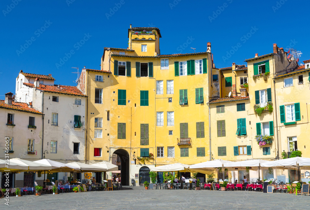 Piazza dell Anfiteatro square in circus yard of medieval town Lucca historical centre, old colorful buildings with shutter windows and blue clear sky background, Tuscany, Italy