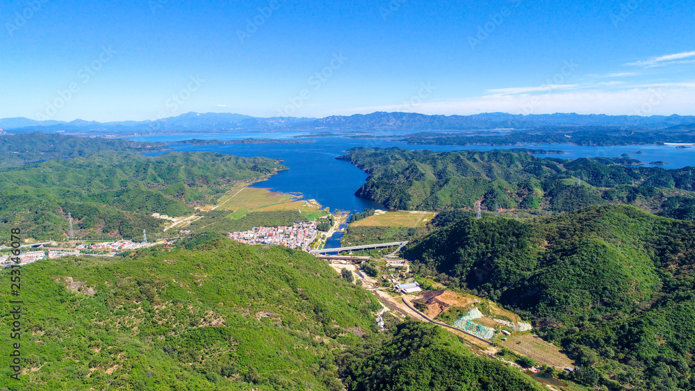 Aerial view of mountain with water reservoir  on the background. Mountain peak with beautiful blue sky and green forest. Landscape of mountain in natural reserve park. Miyun, Beijing, China.