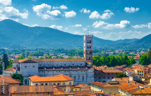 Aerial top panoramic view of Duomo di San Martino San Martin cathedral bell tower in historical centre medieval town Lucca with terracotta tiled roofs and mountain range background, Tuscany, Italy photo