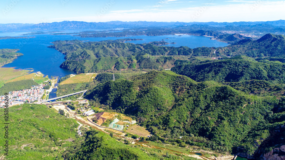 Aerial view of mountain with water reservoir on the background. Mountain peak with beautiful blue sky and green forest. Landscape of mountain in natural reserve park. Miyun, Beijing, China. Aerial view of mountain with water reservoir on the background. Mountain peak with beautiful blue sky and green forest. Landscape of mountain in natural reserve park. Miyun, Beijing, China.