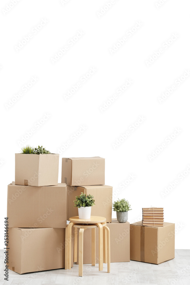Moving to a new home. Belongings in cardboard boxes, books and green plants in pots stand on the gray floor against the background of a white wall. Moving to a new home. Belongings in cardboard boxes, books and green plants in pots stand on the gray floor against the background of a white wall.