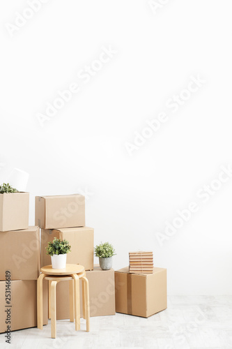 Moving to a new home. Belongings in cardboard boxes, books and green plants in pots stand on the gray floor against the background of a white wall.