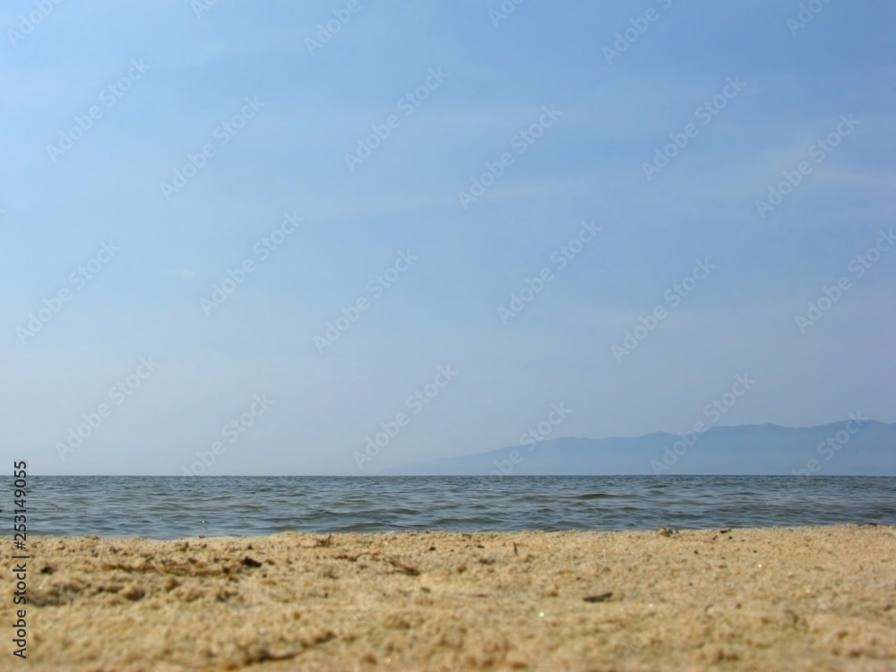 Nobody on the sandy beach, clear sky. Sea background. Low the horizon, silhouette of the mountains.