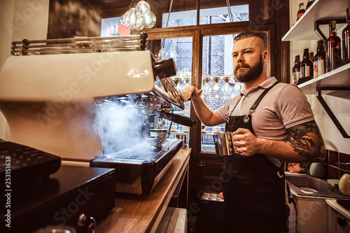 Handsome tattooed barista with stylish beard and hairstyle working on a coffee machine in a coffee shop or restaurant