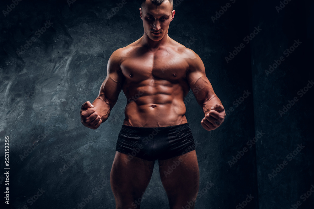 A handsome athletic man in underwear showing his perfect pumped body. Studio photo with dark wall background 