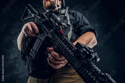 A modern assault rifle in the hands of a soldier special Forces. Close-up and low angle. Studio photo against a dark textured wall