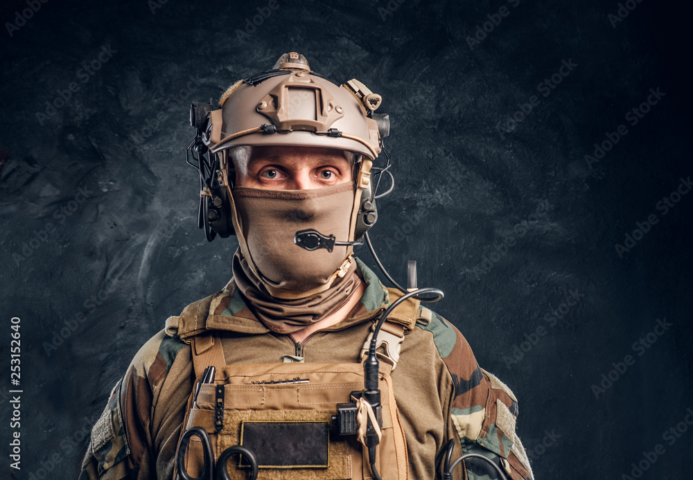 Naklejka premium Close-up portrait. Private security service contractor in camouflage helmet with walkie-talkie. Studio photo against a dark textured wall