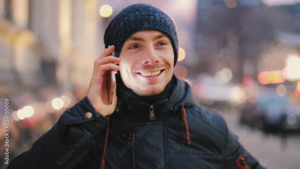 Happy smiling man talks by smartphone walking in a night city street Happy smiling man talks by smartphone walking in a night city street