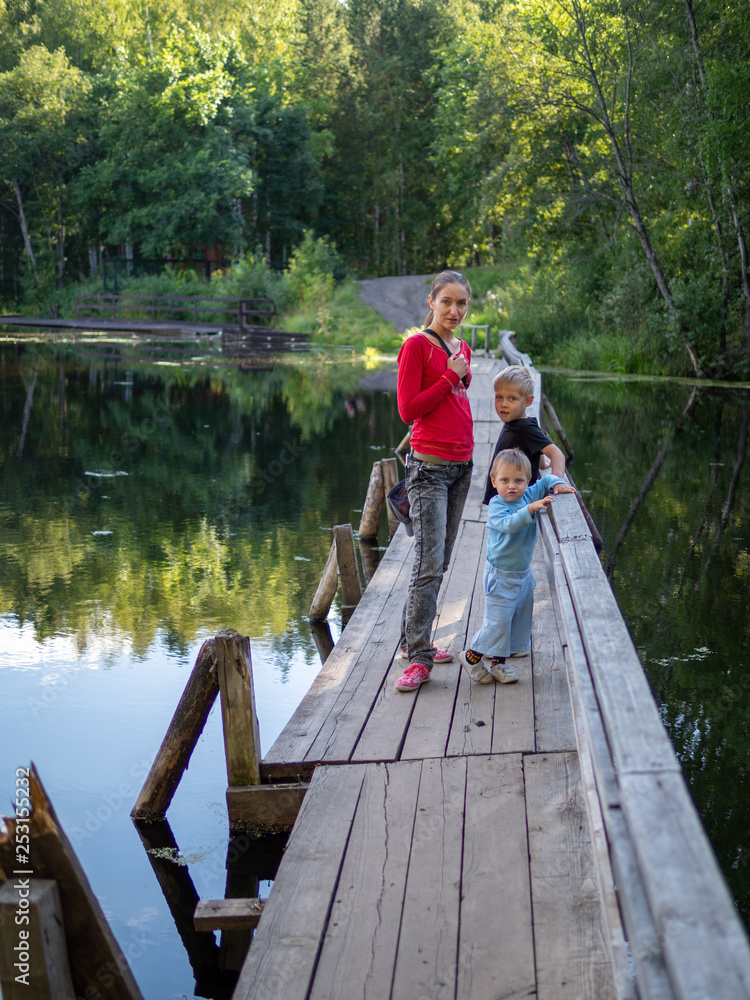 A girl with two children are standing on the old wooden bridge across a quiet river A girl with two children are standing on the old wooden bridge across a quiet river