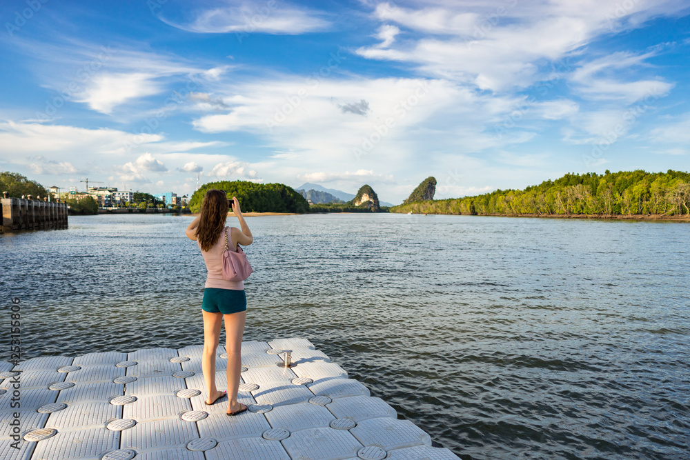 Woman tourist takes photo of Khao Khanab Nam mountains on smartphone on river in Krabi town in Thailand Woman tourist takes photo of Khao Khanab Nam mountains on smartphone on river in Krabi town in Thailand