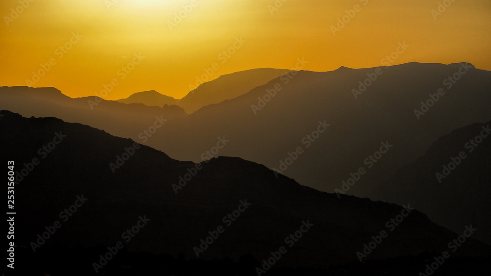 Silhouettes of mountains against the background of the sun. Ru'us al Jibal. Al Hajar Moutains. Musandam. Oman