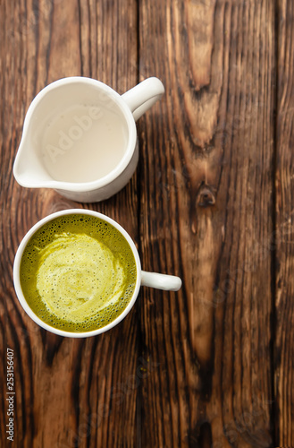 cup of hot matcha green tea latte and cup of milk on wood background