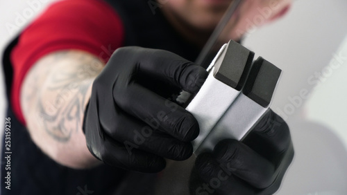 A professional worker guy (Male) applies ceramics (special liquid) to the car using an applicator (sponge) in black gloves and in a protective robe. Concept of: Auto service, Deteyling. photo