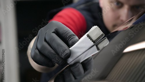A professional worker guy (Male) applies ceramics (special liquid) to the car using an applicator (sponge) in black gloves and in a protective robe. Concept of: Auto service, Deteyling. © dkHDvideo