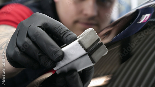 A professional worker guy (Male) applies ceramics (special liquid) to the car using an applicator (sponge) in black gloves and in a protective robe. Concept of: Auto service, Deteyling.